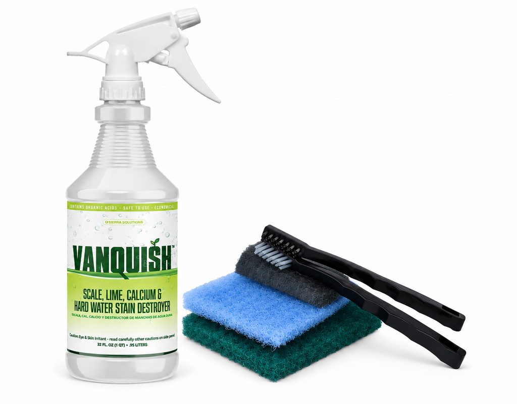 A Vanquish hard water stain destroyer cleaning kit on a white background, featuring a clear spray bottle with a white trigger sprayer and a green-and-white label, alongside two black cleaning brushes resting on stacked blue and green scouring pads.